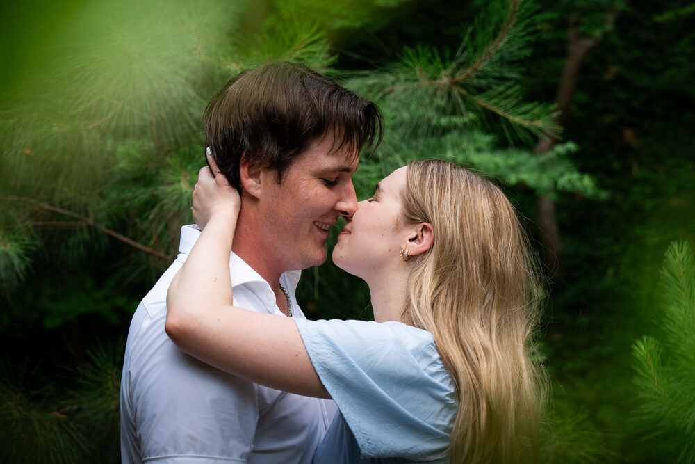 Joshua and Hailey leaning in close together, framed by soft green pine boughs