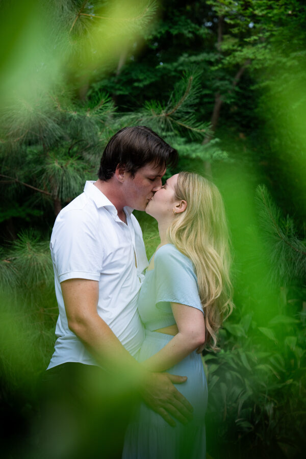 Joshua and Hailey kissing, framed by out-of-focus pine branches