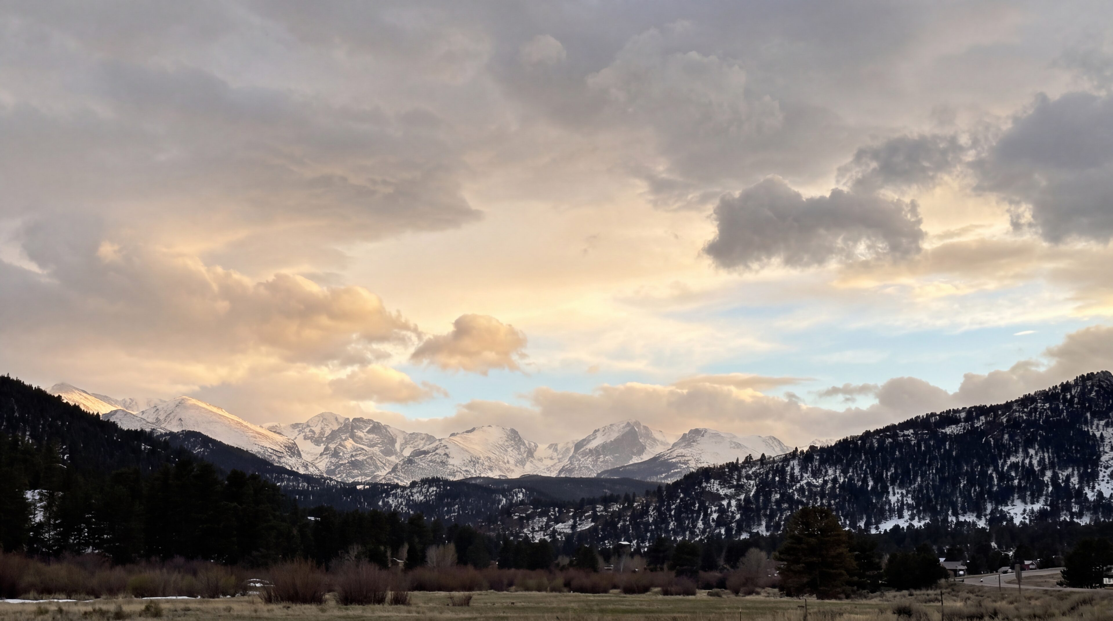 Snow-capped peaks of the Rocky Mountains under a warm evening sky of gold and blue above Estes Park, Colorado