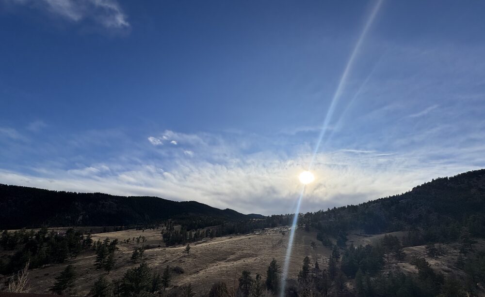 Sun breaking over a wide Colorado valley of golden meadow and dark evergreen ridgelines