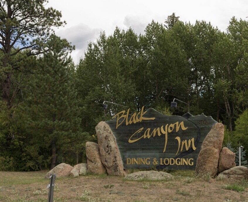 The carved Black Canyon Inn sign, Dining & Lodging, set among boulders and pines